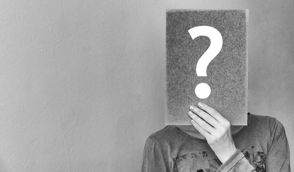 Person holding a large card with a question mark obscuring their face against a plain background.