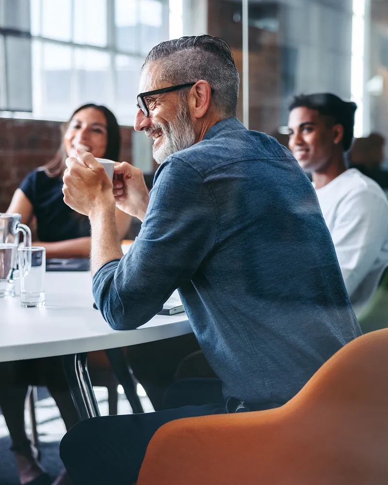 Group of diverse people having a casual meeting at a modern office, with one person holding a coffee cup and smiling.