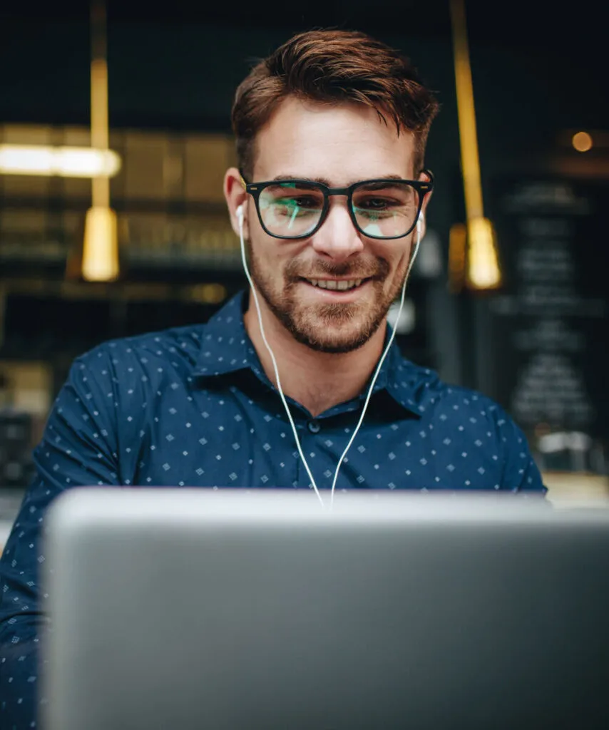 Young man with glasses and earphones working on a laptop in a modern workspace.