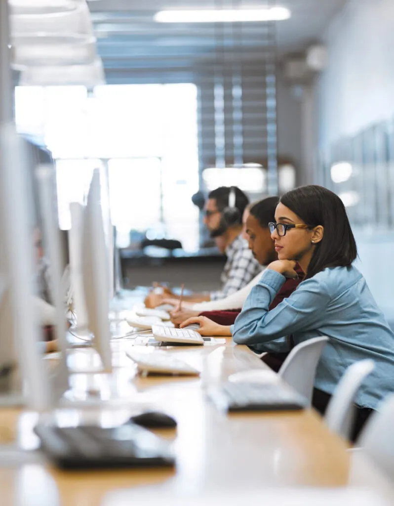 People working on computers in a bright office environment, focused and engaged in their tasks.