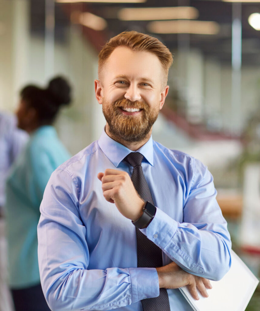 Smiling man in blue shirt with cross-armed pose in modern office environment.