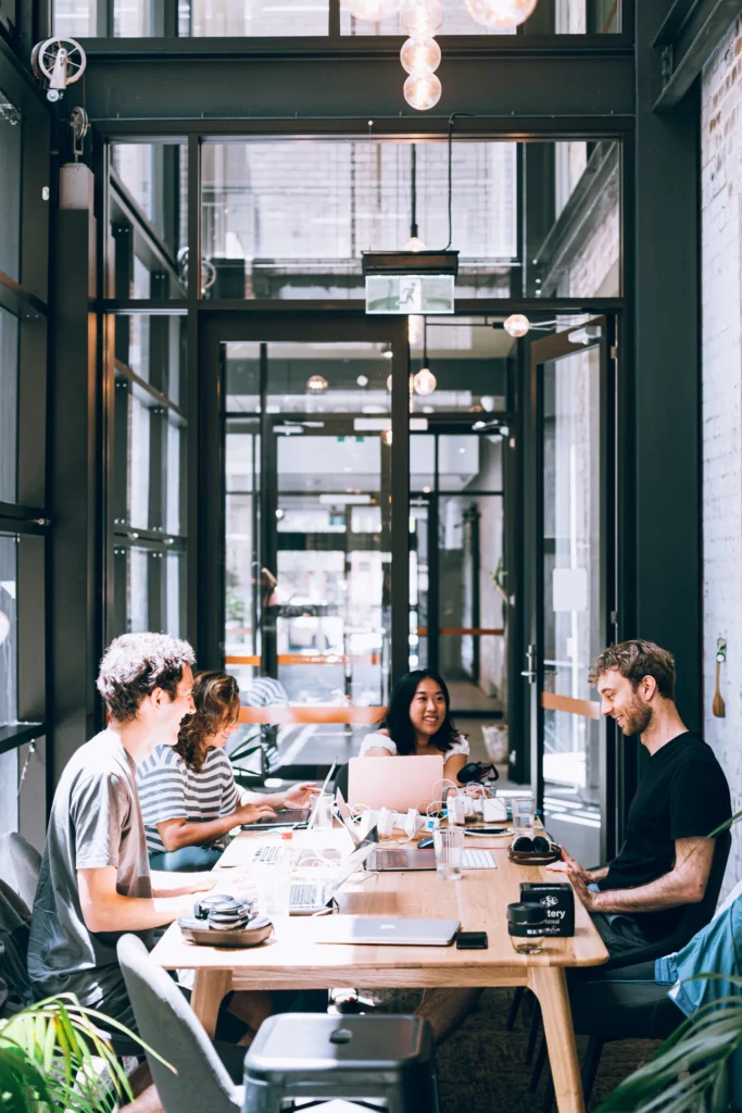 Colleagues collaborate in a sunlit office space with laptops on a wooden table.