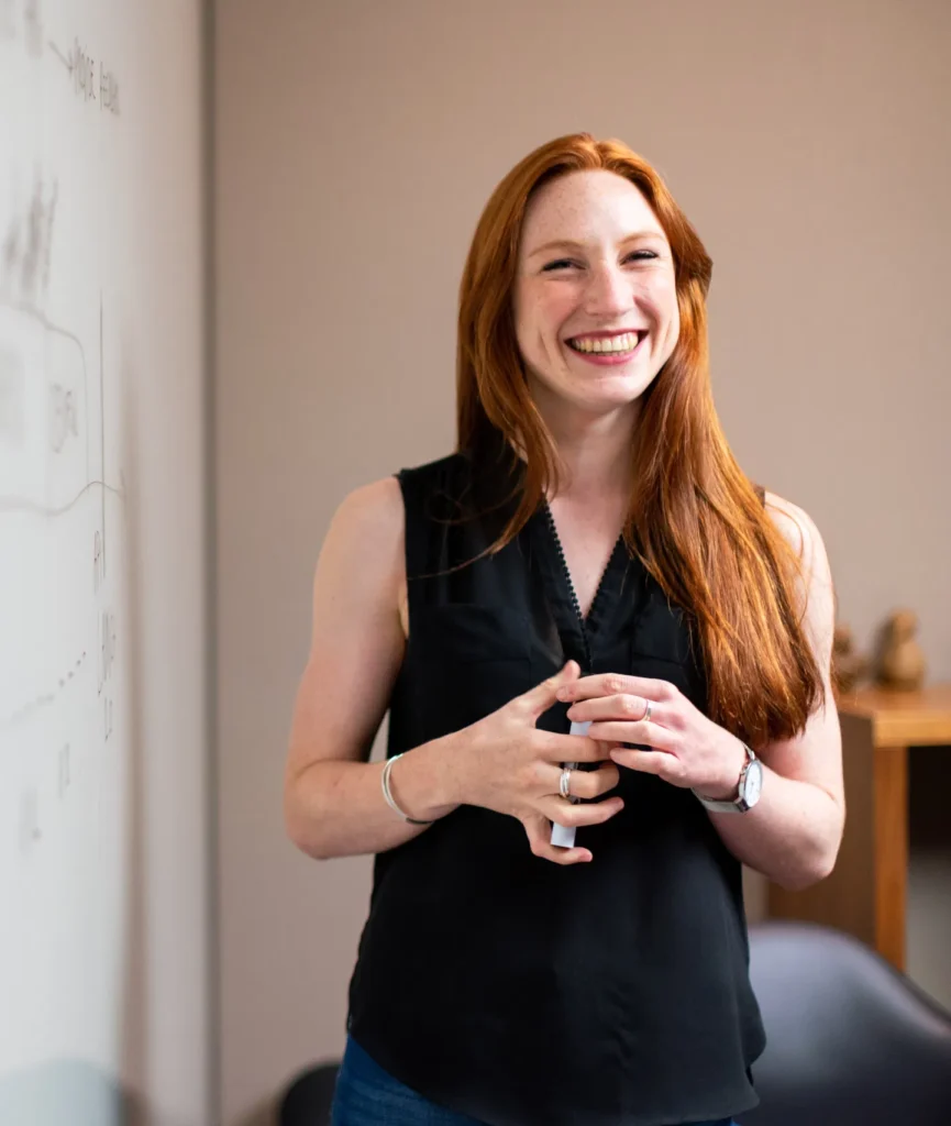 Smiling woman giving presentation, standing by a whiteboard with diagrams.
